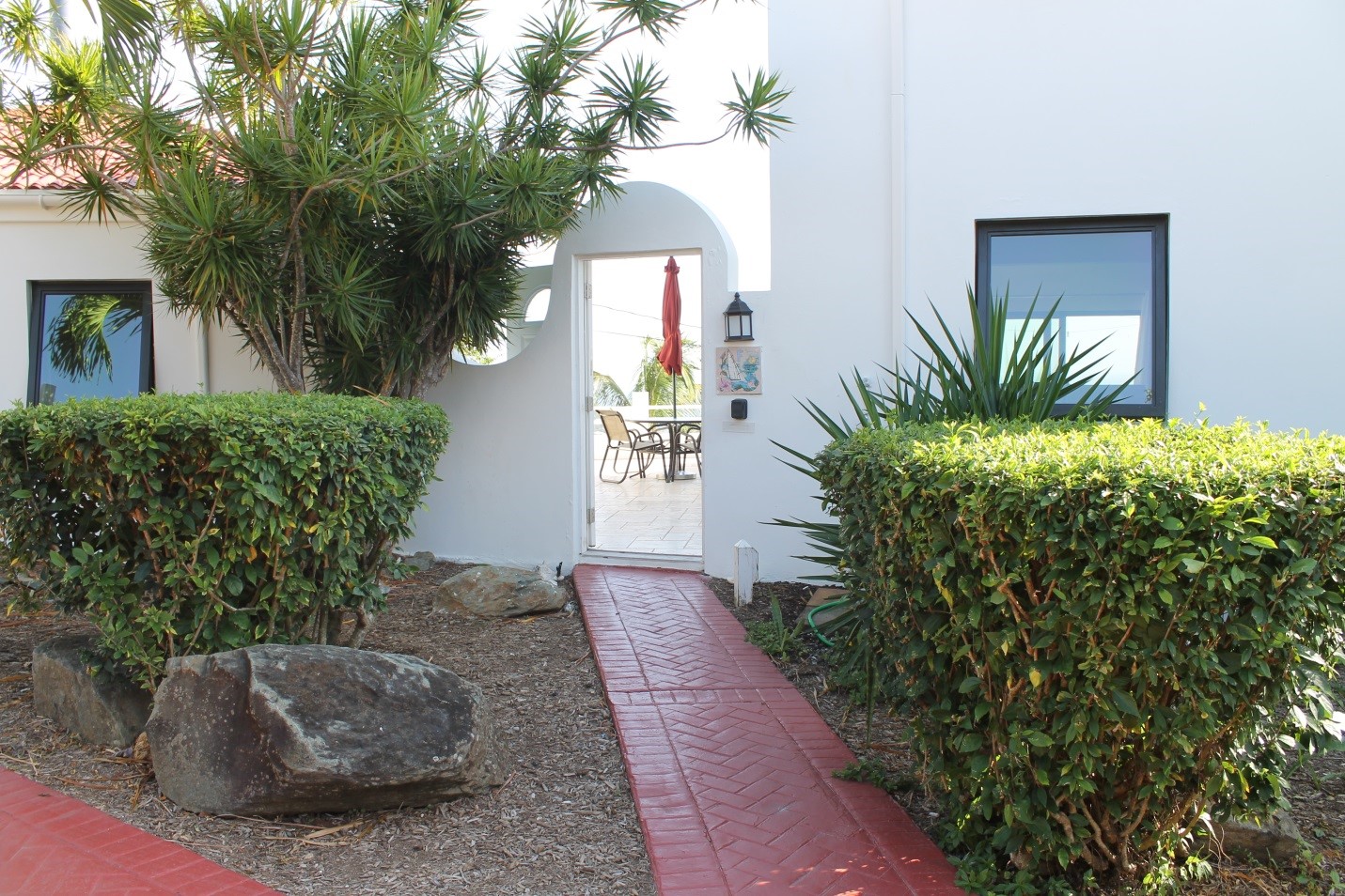 A white door way with bushes and plants in the background.